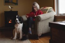 Donna che utilizza tablet digitale con cane seduto accanto a lei in soggiorno — Foto stock