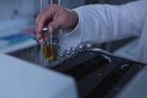 Nahaufnahme eines männlichen Wissenschaftlers, der eine Chemieflasche auf eine Maschine legt — Stockfoto
