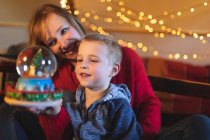 Mother and son holding Christmas tree snow globe at home — Stock Photo