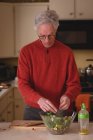 Старший мужчина готовит салат на кухне дома — стоковое фото