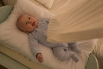 Niño sonriendo mientras se relaja en la cama de bebé en casa - foto de stock