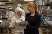 Female manager and female chefs discussing over clipboard in kitchen — Stock Photo