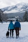 Вид ззаду пари з собакою, що йде на сніговий пейзаж — стокове фото