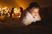 Посміхається дівчина, використовуючи цифровий планшетний проти Різдвяні вогні — стокове фото