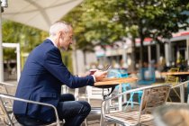 Вид сбоку бизнесмена, пользующегося мобильным телефоном в открытом кафе — стоковое фото