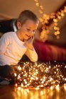 Niño sonriente mirando luces de hadas iluminadas en casa - foto de stock