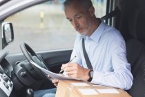 Side view of delivery man writing on paper in delivery van — Stock Photo