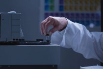 Мужчина-ученый помещает стеклянную бутылку химической трубки на машину в лаборатории — стоковое фото