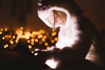 Fille en veste à capuche en utilisant une tablette numérique contre les lumières de Noël — Photo de stock