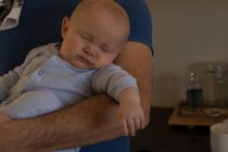 Bébé garçon dormir dans son père bras à la maison — Photo de stock