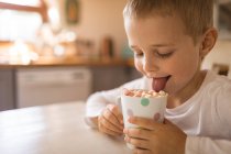Verschmitzter Junge leckt eine Tasse voll Marshmallows — Stockfoto
