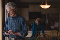 Senior utilisant un téléphone portable à la maison — Photo de stock