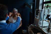 Оптометрист осматривает глаза пациента с помощью оборудования для проверки зрения в клинике — стоковое фото