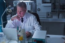 Científico masculino reflexivo usando el ordenador portátil en el laboratorio - foto de stock