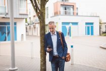 Uomo d'affari che utilizza il telefono cellulare in città in una giornata di sole — Foto stock