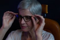Primer plano de la mujer mayor ajustando anteojos en la clínica - foto de stock