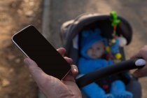 Pai usando telefone celular com bebê menino no carrinho no parque — Fotografia de Stock