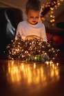 Neugieriger Junge schaut zu Hause auf beleuchtete Lichterketten — Stockfoto