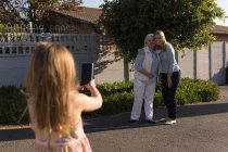 Hija tomando fotos de su madre y abuela con teléfono móvil en el jardín - foto de stock