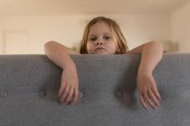 Retrato de niña de pie detrás del sofá en la sala de estar en casa - foto de stock