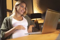 Nahaufnahme einer schwangeren Frau, die zu Hause mit dem Laptop lächelt — Stockfoto