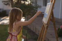 Side view of girl painting on canvas in the garden — Stock Photo
