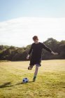 Jugador de fútbol pateando fútbol en el campo en un día soleado - foto de stock