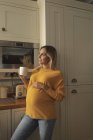 Mujer embarazada sonriente con taza de café de pie en la cocina - foto de stock