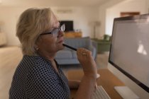 Старшая женщина, работающая дома за компьютером — стоковое фото