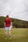 Vista trasera del jugador de rugby de pie con pelota de rugby en el campo - foto de stock
