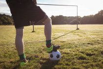 Baixa seção de jogador de futebol de pé com bola de futebol no campo — Fotografia de Stock