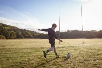 Jugador de rugby pateando pelota de rugby en el campo en un día soleado - foto de stock