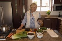 Старшая женщина ищет рецепт на цифровой планшет на кухне дома — стоковое фото