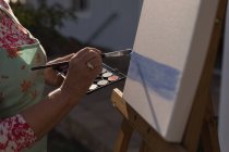 Close-up of senior woman painting on canvas in the garden — Stock Photo