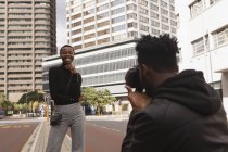 Hombre tomando fotos de mujer feliz con tableta digital en la calle de la ciudad - foto de stock