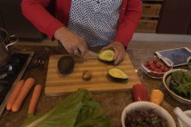 Donna anziana che taglia avocado in cucina a casa — Foto stock