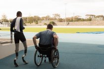 Вид сзади на двух спортсменов-инвалидов, идущих вместе по спортивному объекту — стоковое фото