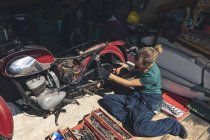 Vista de alto ângulo da mecânica feminina reparando moto na garagem — Fotografia de Stock