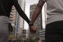Mid Section of couple walking hand in hand in city street — Stock Photo