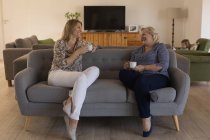 Мать и дочь взаимодействуют друг с другом за чашечкой кофе в гостиной дома — стоковое фото