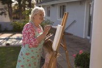 Side view of senior woman painting on canvas in the garden — Stock Photo