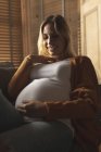 Smiling pregnant woman sitting on sofa touching her belly — Stock Photo