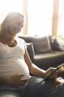 Donna incinta sorridente con tablet digitale sul divano — Foto stock
