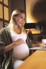 Усміхнена вагітна жінка використовує ноутбук вдома — стокове фото