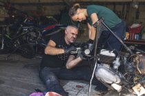 Mecanicistas masculinos y femeninos reparando motocicleta en garaje de reparación - foto de stock
