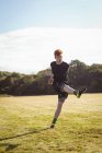 Футболист, пинающий футбол в поле в солнечный день — стоковое фото