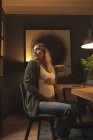 Femme enceinte regardant derrière tout en utilisant un ordinateur portable à la maison — Photo de stock