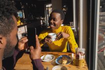 Счастливый мужчина фотографирует женщину в кафе — стоковое фото