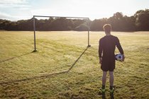Vista trasera del jugador de fútbol de pie con pelota de fútbol en el campo - foto de stock