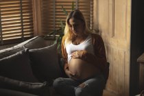 Schwangere sitzt auf Sofa und berührt ihren Bauch zu Hause — Stockfoto